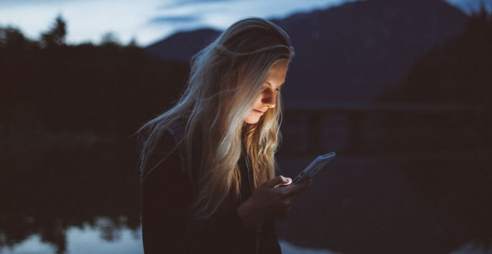 woman scrolls phone in nature at night