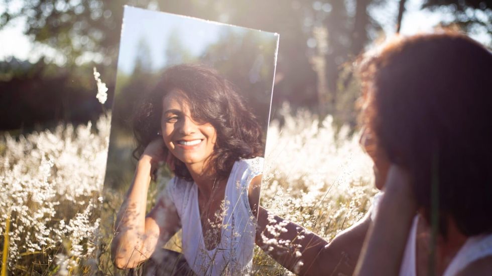 woman smiling, holding, and looking into a mirror
