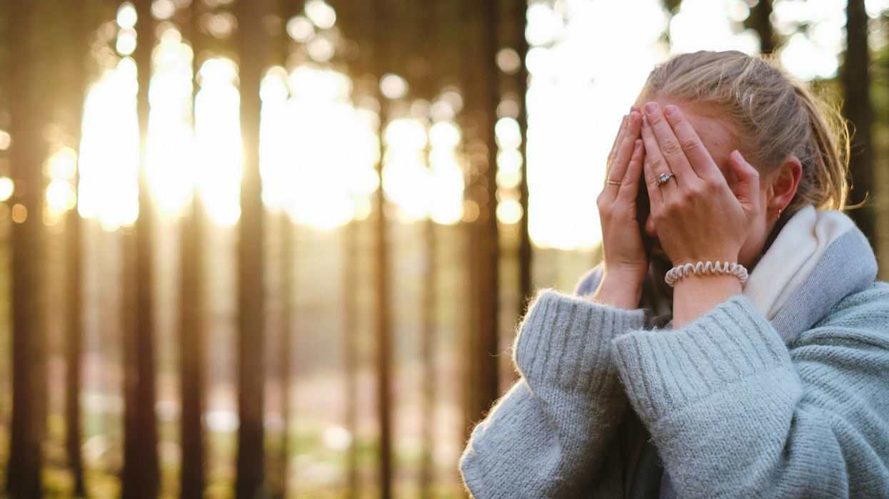 Woman wearing a gray outfit with her hands covering her face.