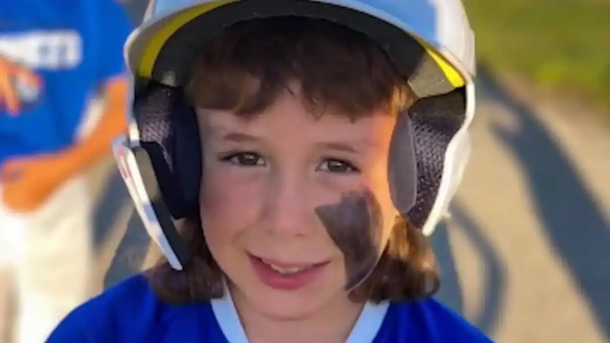 young boy smiles with face paint and baseball helmet on.