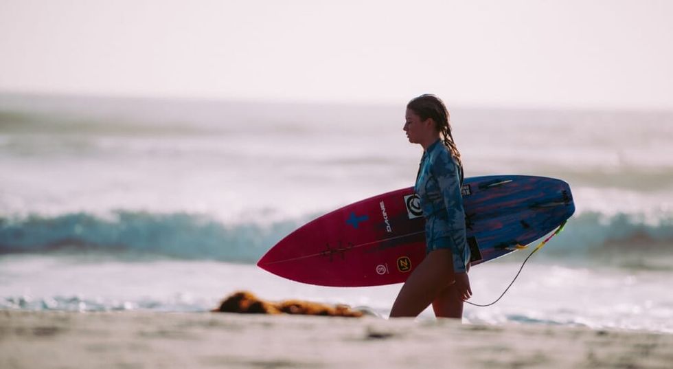 young girl holds surfboard on beach