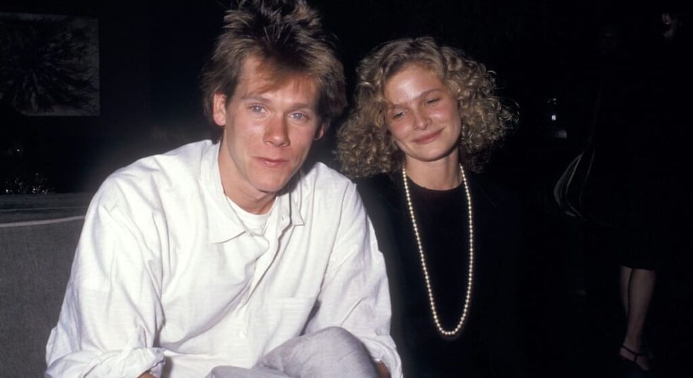 Young Kevin Bacon and wife Kyra Sedgwick at a club smiling at the camera.