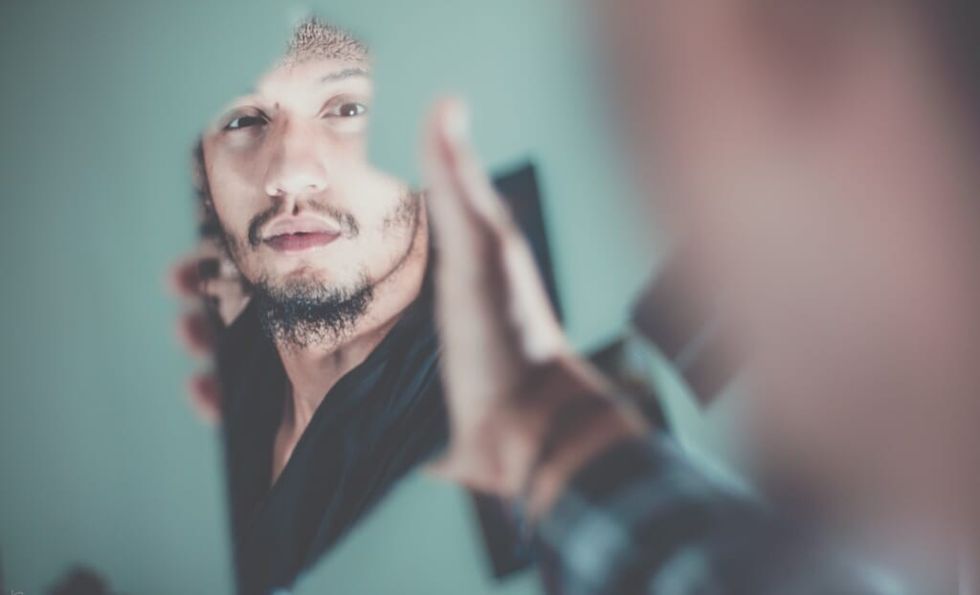 young man with facial hair looks in broken mirror