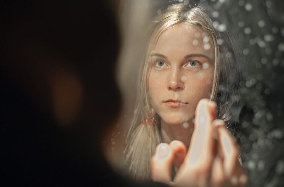 young woman looks at her reflection in mirror