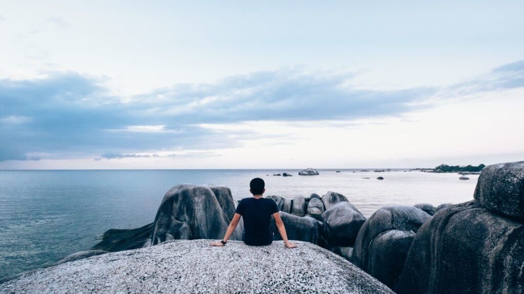 man sitting on rock looking out at the sea