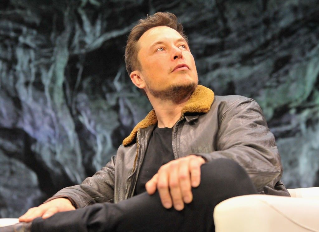 Elon Musk answering questions at a conference wearing a leather jacket.
