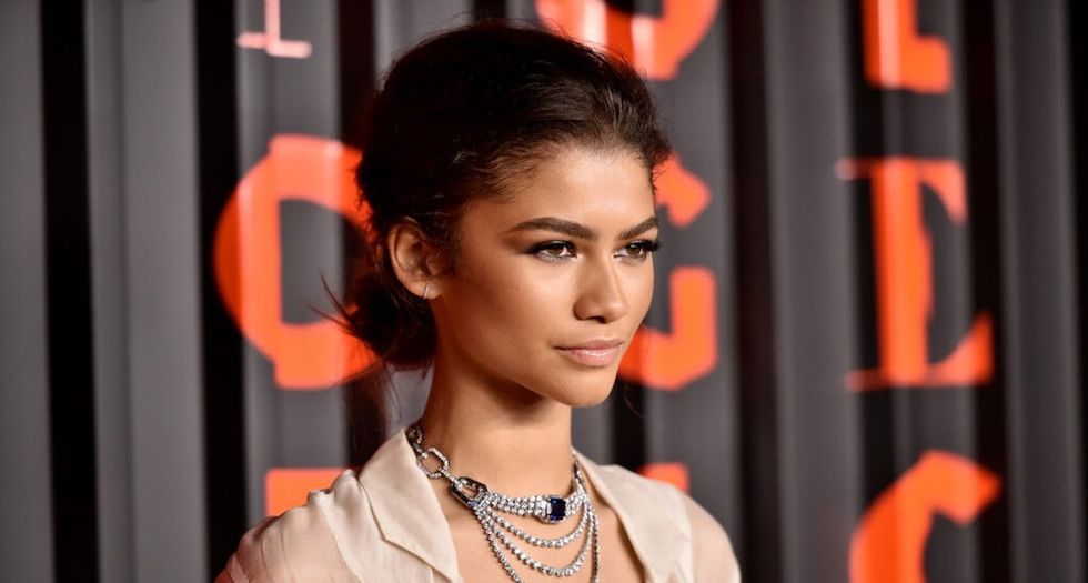 Zendaya in beige dress and silver jewelry standing on the red carpet.