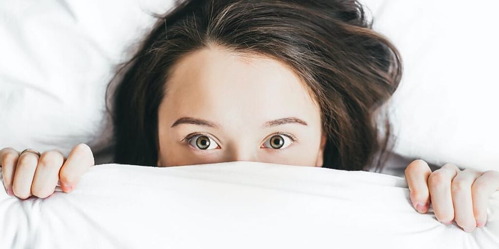 Girl in bed holding sheets over half of her face by Alexandra Gorn on Unsplash