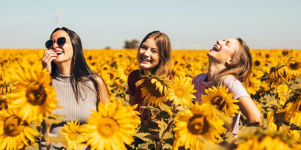 Trei femei fericite, zâmbind într-un câmp de floarea-soarelui de Antonino Visalli pe Unsplash