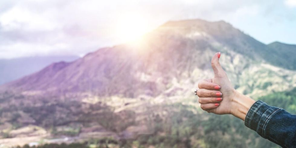 Woman making thumbs up sign with hand in front of mountainview by Artem Beliaikin on Unsplash