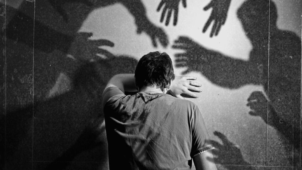 Man leaning face on wall with shadow of hands reaching towards him