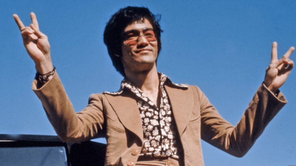 Bruce Lee doing peace signs in tan 70s suit