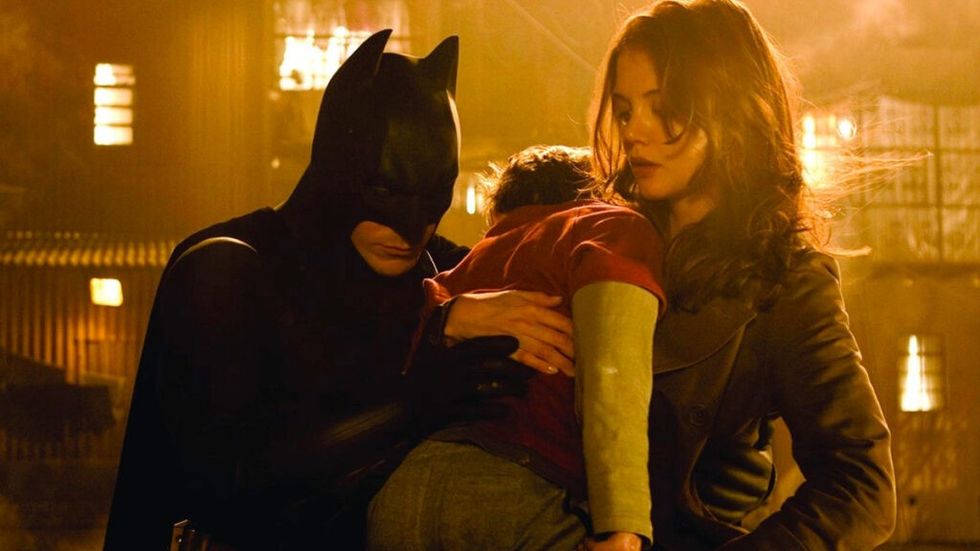 Christian Bale as Batman and Katie Holmes hold bvoy in Batman Begins