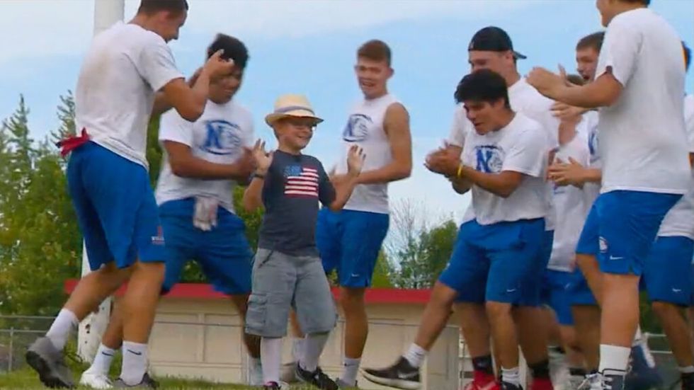 High School football team cheers on young boy in American Flag shirt