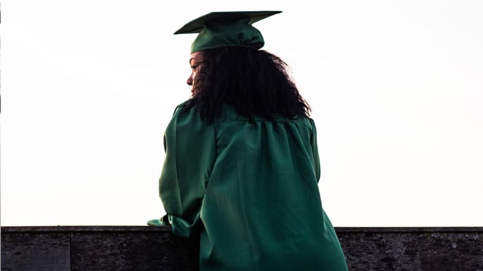 Black woman graduate in green cap and gown looks over ledgeBlack woman graduate in green cap and gown looks over ledge