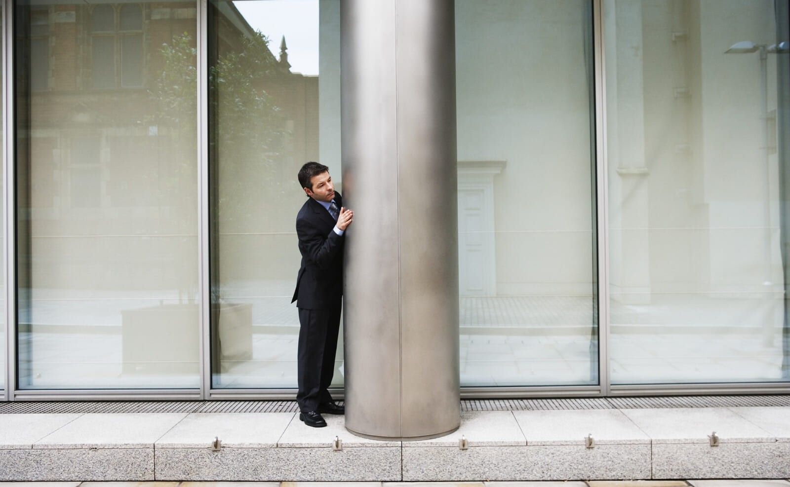 Paranoid businessman standing by column on exterior of building