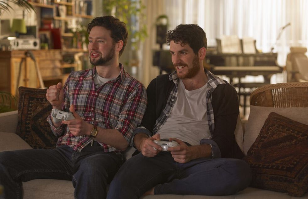 Two young man sitting on the sofa playing video games, One of them is celebrating