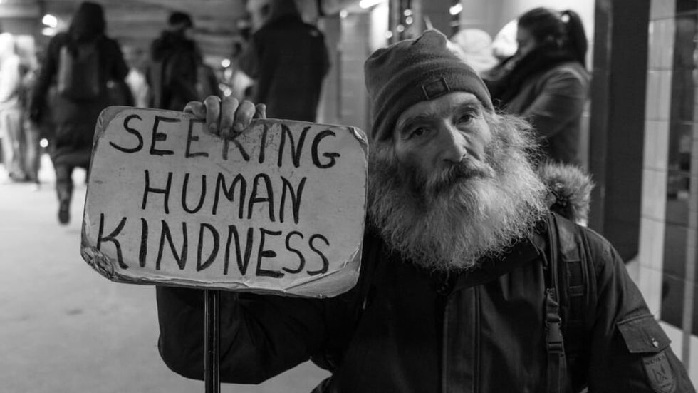 Homeless man holding Human Kindness sign