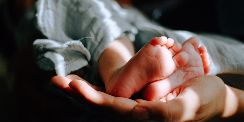 Piciorul copilului în palma mâinii persoanei