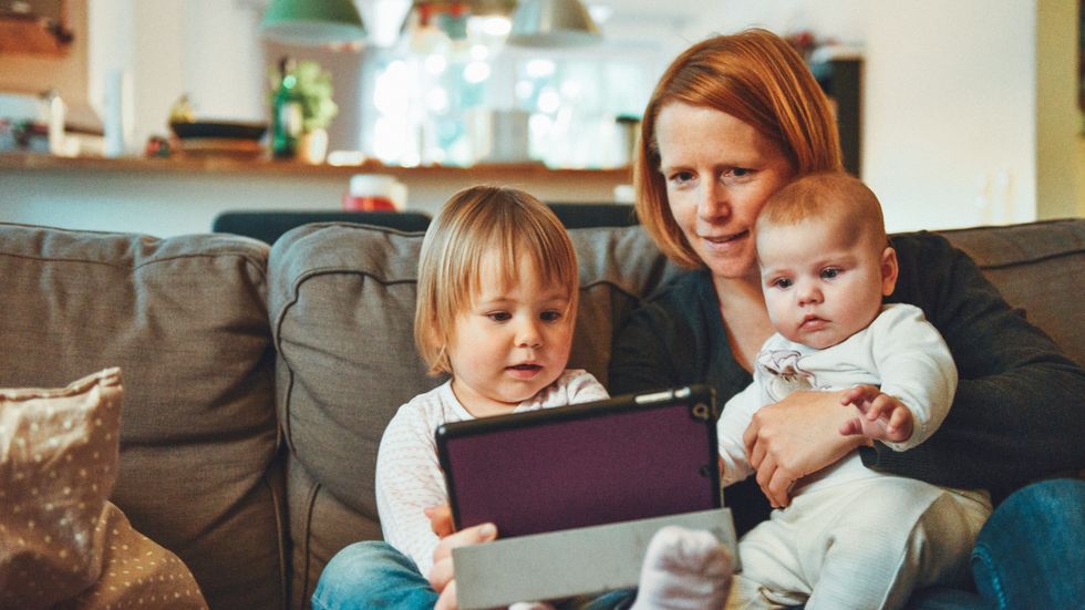 mom and 2 kids holding an iPad on a couch