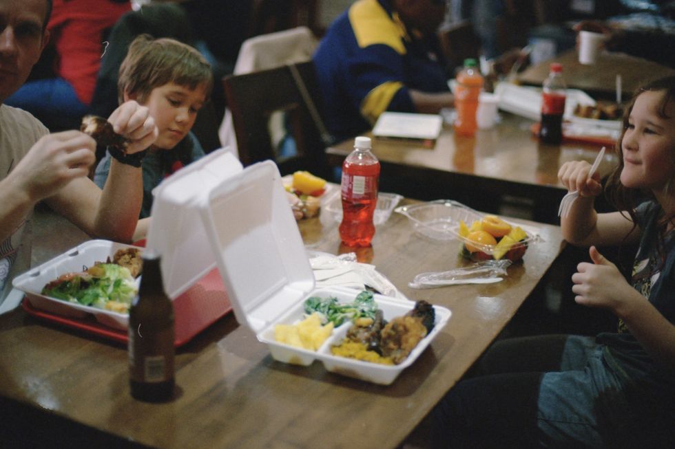 food in white containers on a table surrounded by 3 people 