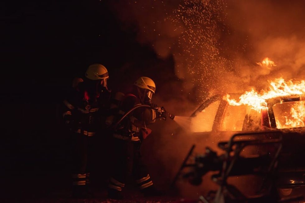 two firefighters spraying a burning car with water