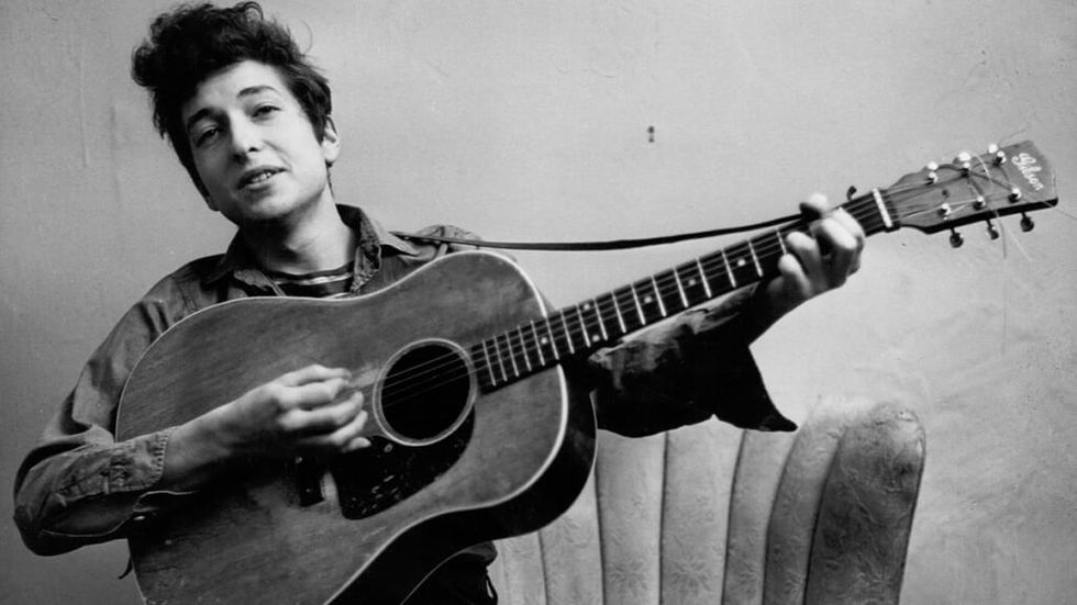 Tânărul Bob Dylan alb-negru cântând la chitară acustică