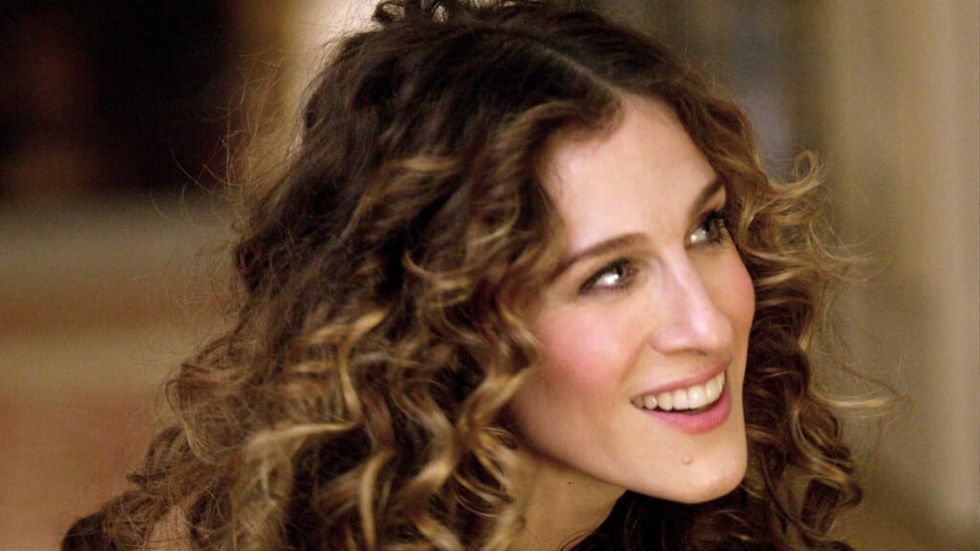 Carrie from Sex in the City with curly hair smiling off camera