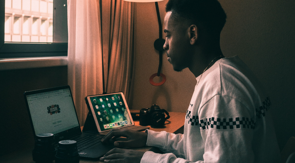 Un bărbat care stă la un birou înconjurat de tehnologie - computer, iPad și iPhone