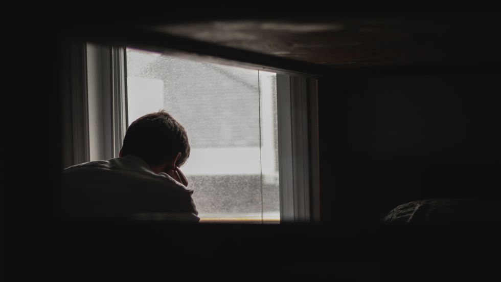 depressed man struggles beside window in dark room