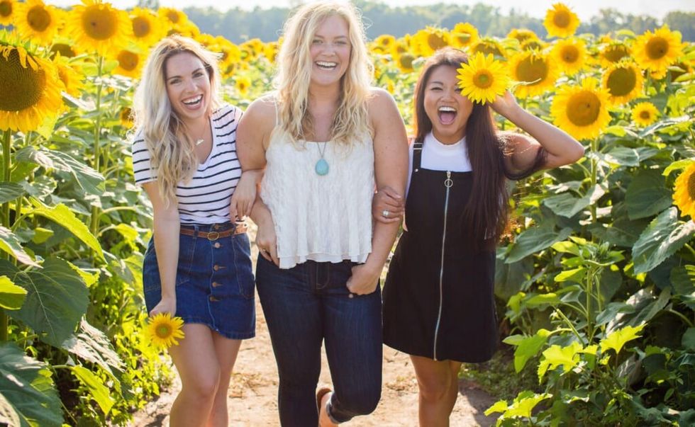 three young woman in a field with sunflowers