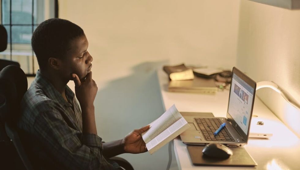 Un adult care citește o carte stând la birou în fața laptopului
