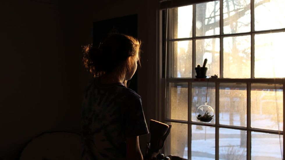 O femeie care stă într-o cameră întunecată în fața unei ferestre iluminate 