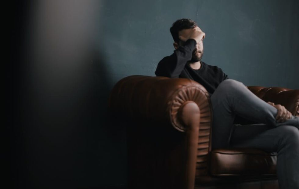 depressed young man sits on couch holding face