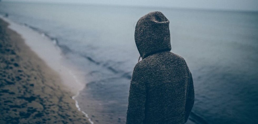 young person walks in hoodie on the beach