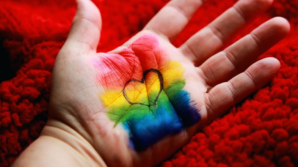 pride flag with a outline of a heart painted on a person's palm