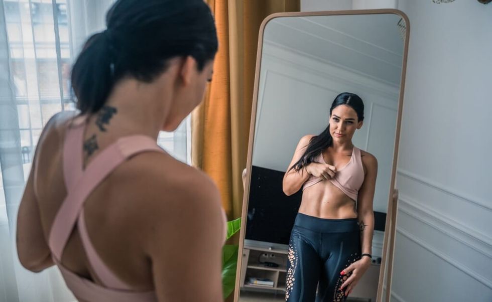 young woman looks at her body in the mirror