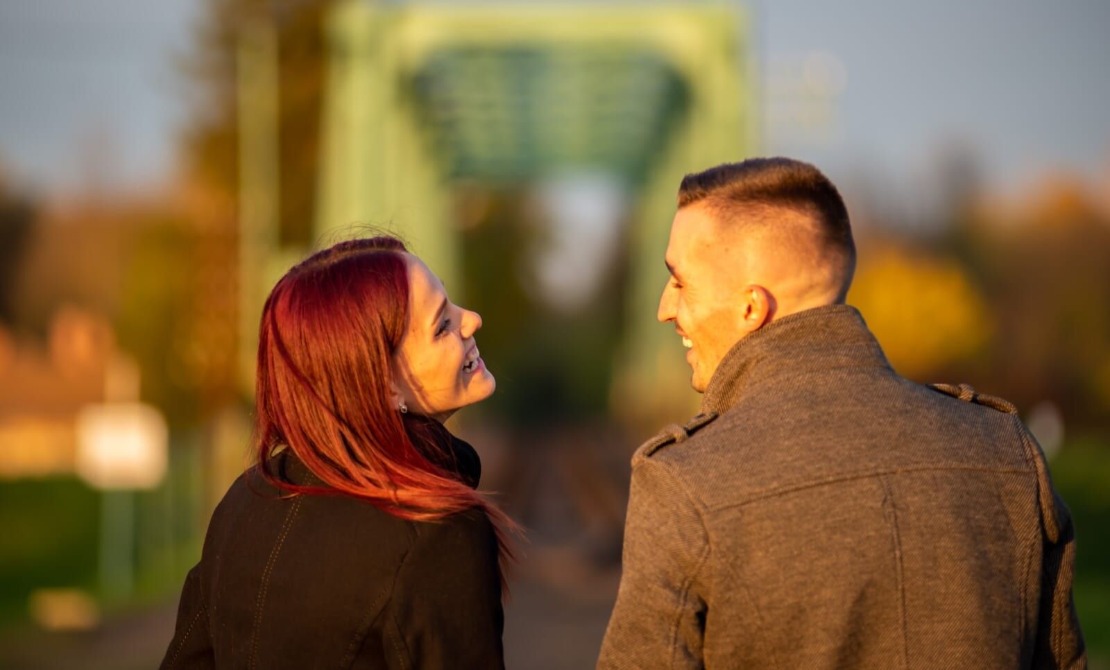 couple flirts on date in front of green bridge