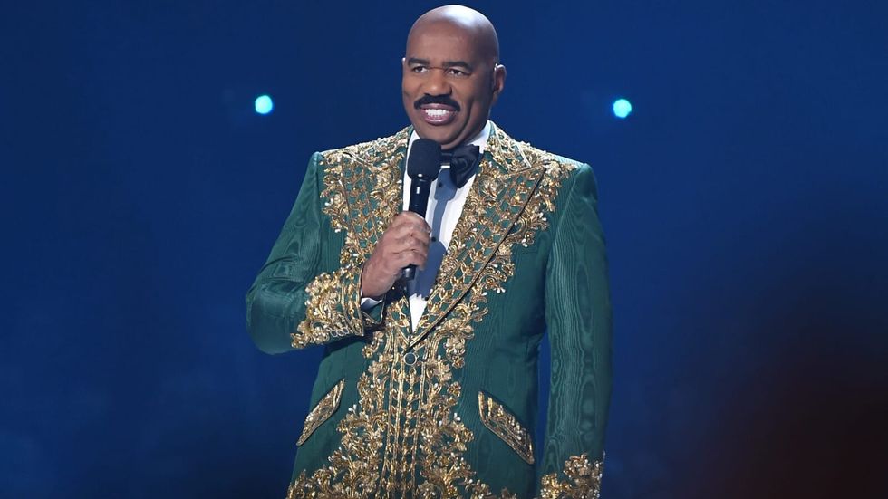 man wearing a green suit with gold detailing, holding a mic