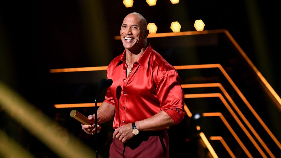 Un bărbat într-o cămașă roșie și pantaloni, ținând un premiu pe scenă