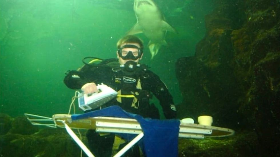 Scuba diver irons clothes underwater with sharks