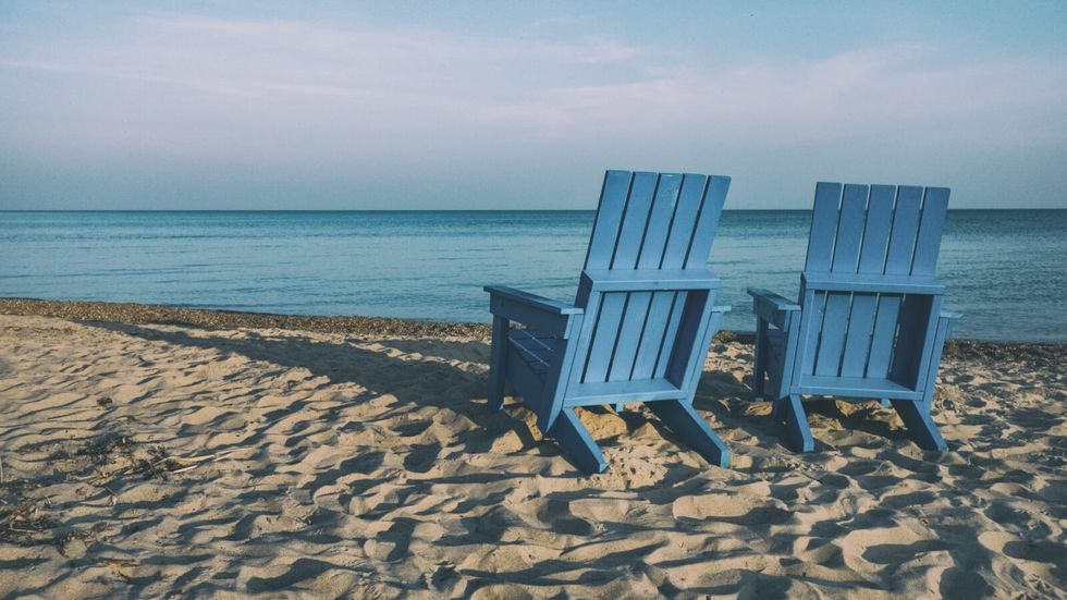 2 blue chairs on the sand on a beach