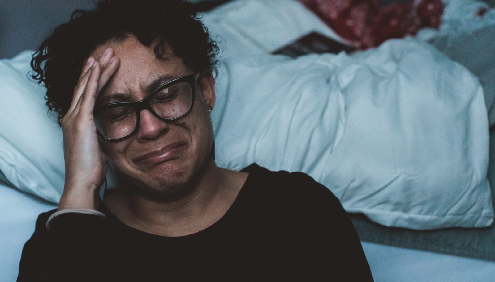 woman cries on the floor leaning against bed