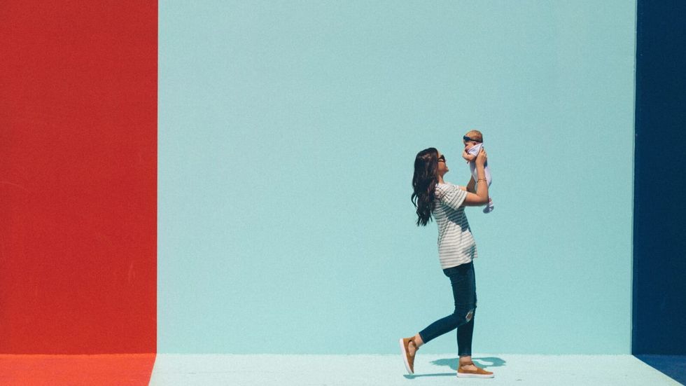 woman carrying a baby in front of a red and blue wall