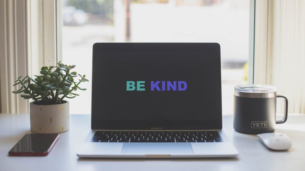 laptop on a desk containing the screensaver "be kind"