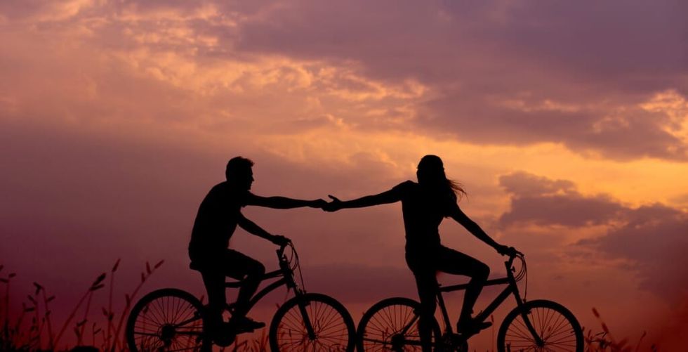 a couple reaches for one another on bicycles