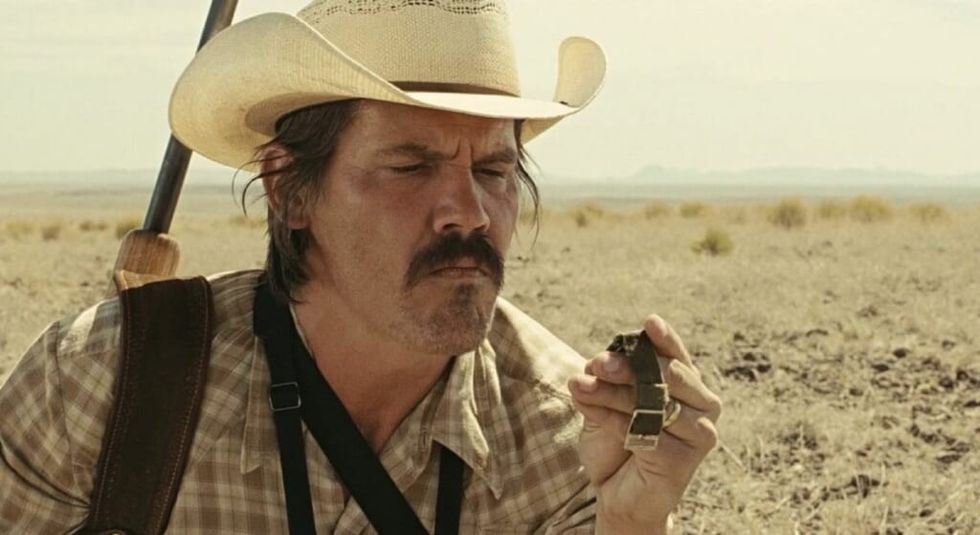 Josh Brolin in No Country For Old Men in the desert looking at a watch.
