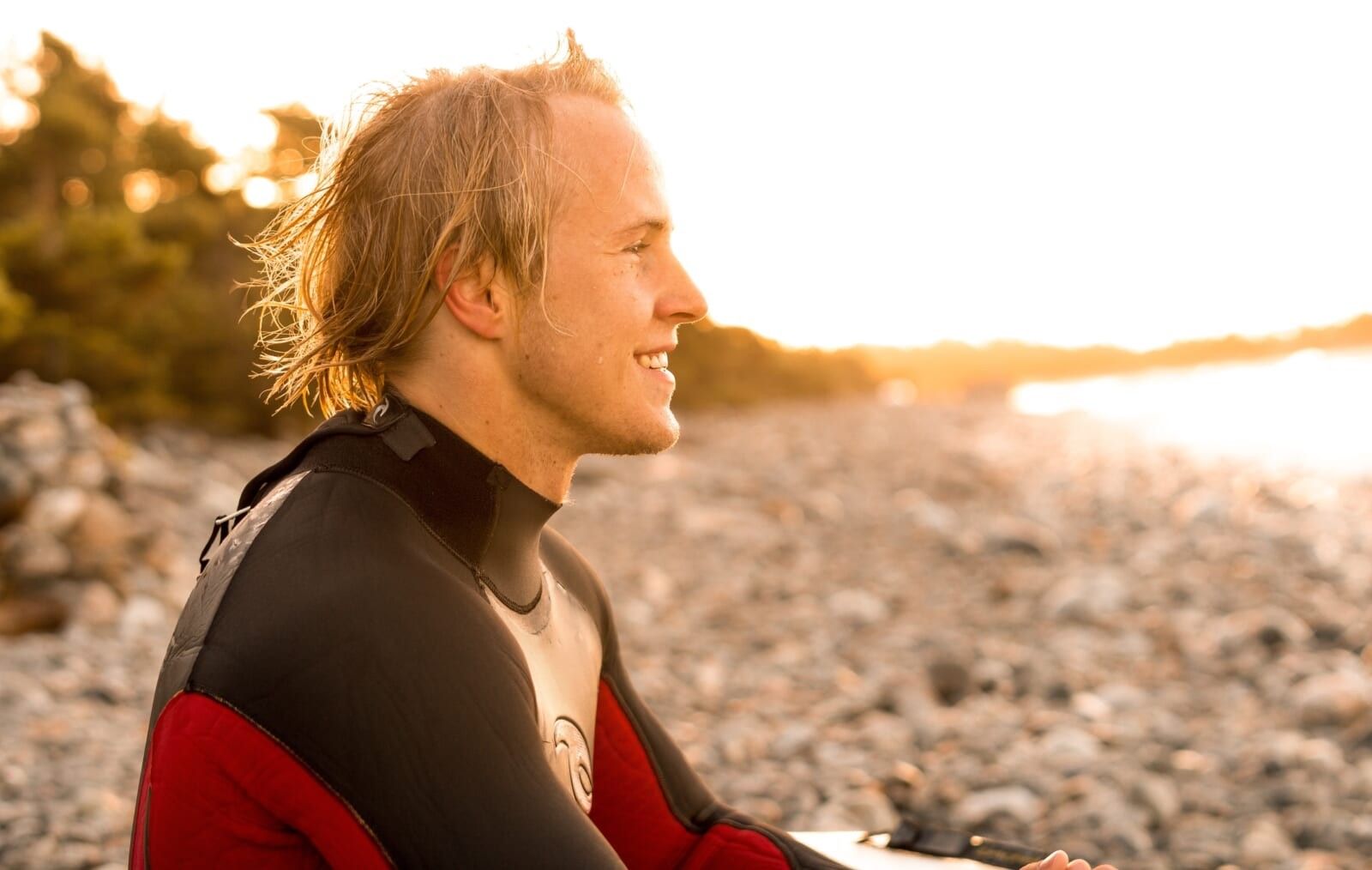 young man sits in wetsuit on the beach