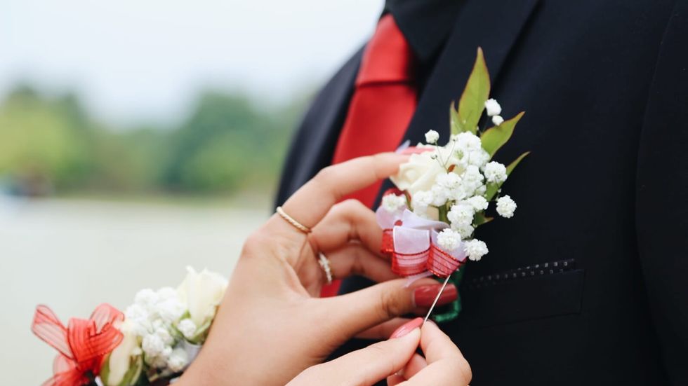 person pinning a corsage on a man's tuxedo