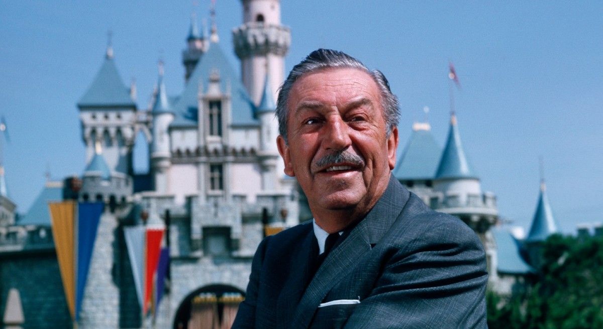 Walt Disney posing in front of Disney castle.